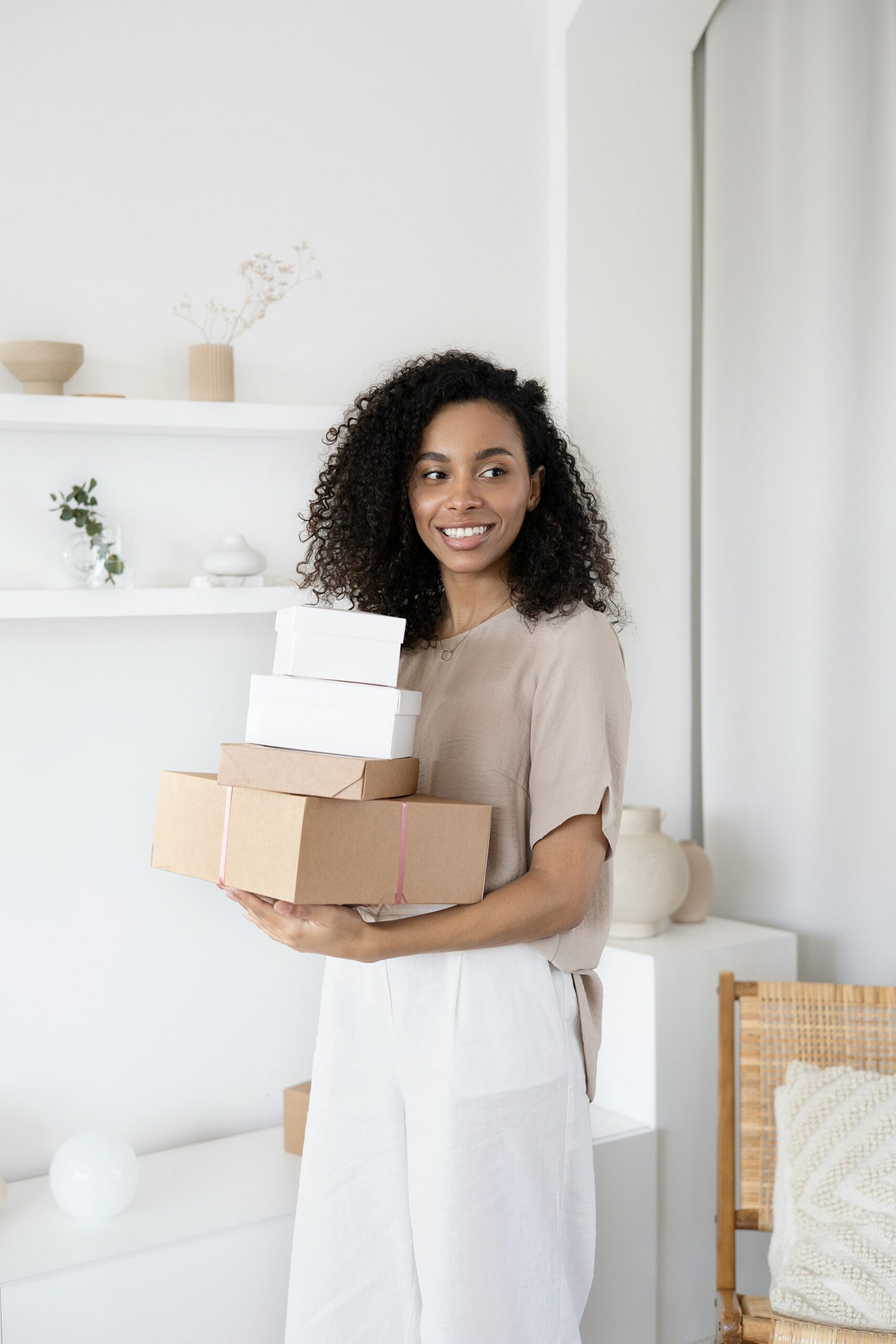 Young African American woman smiling while holding cardboard boxes indoors.